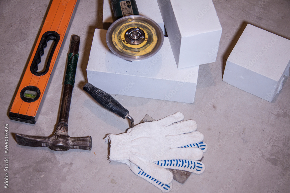 Composition tools for the construction and repair of buildings. Set on a plaster background. Level tool, grinder, bricks and hammer with white gloves. Equipment for the bricklayer