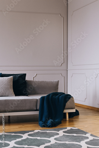 Blue blanket and pillows on grey comfortable sofa in designed living room interior with wooden floor and white wall