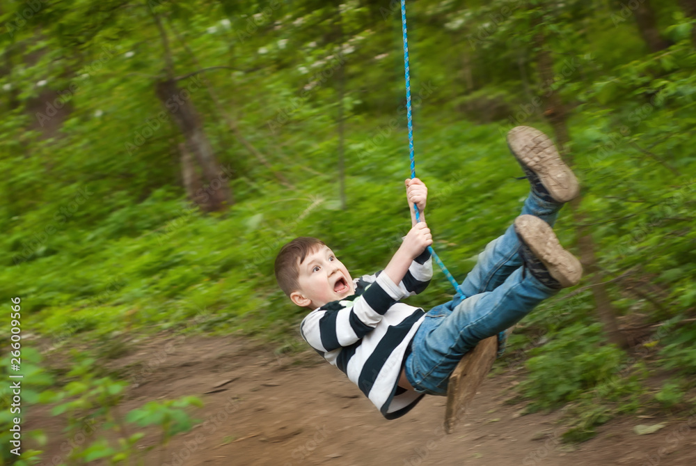 Children are riding a swing in the park. Guys on a homemade swing from ropes and boards. Light blur as an artistic effect of motion.