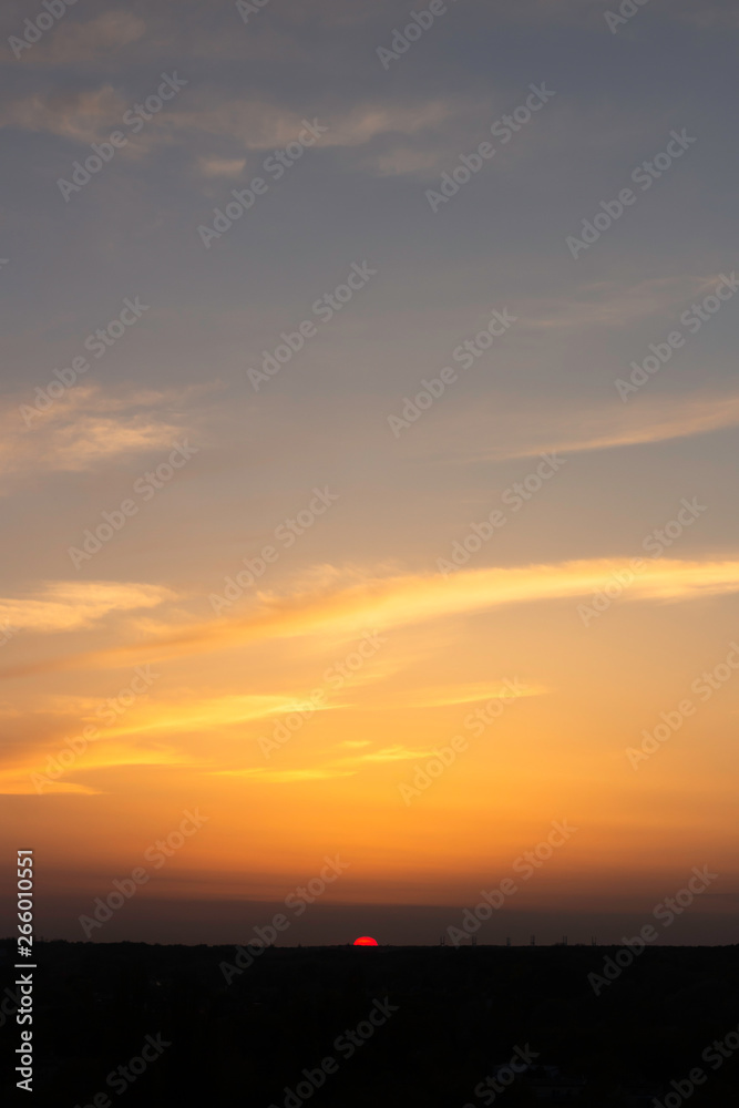 the pink sun sets over the city skyline, illuminating the orange clouds