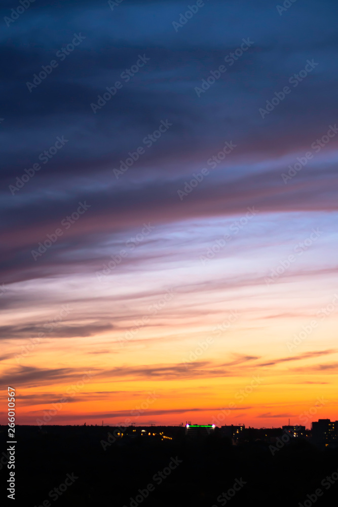 sunset sky blue-orange colors with dramatic clouds against the bokeh lights of the city