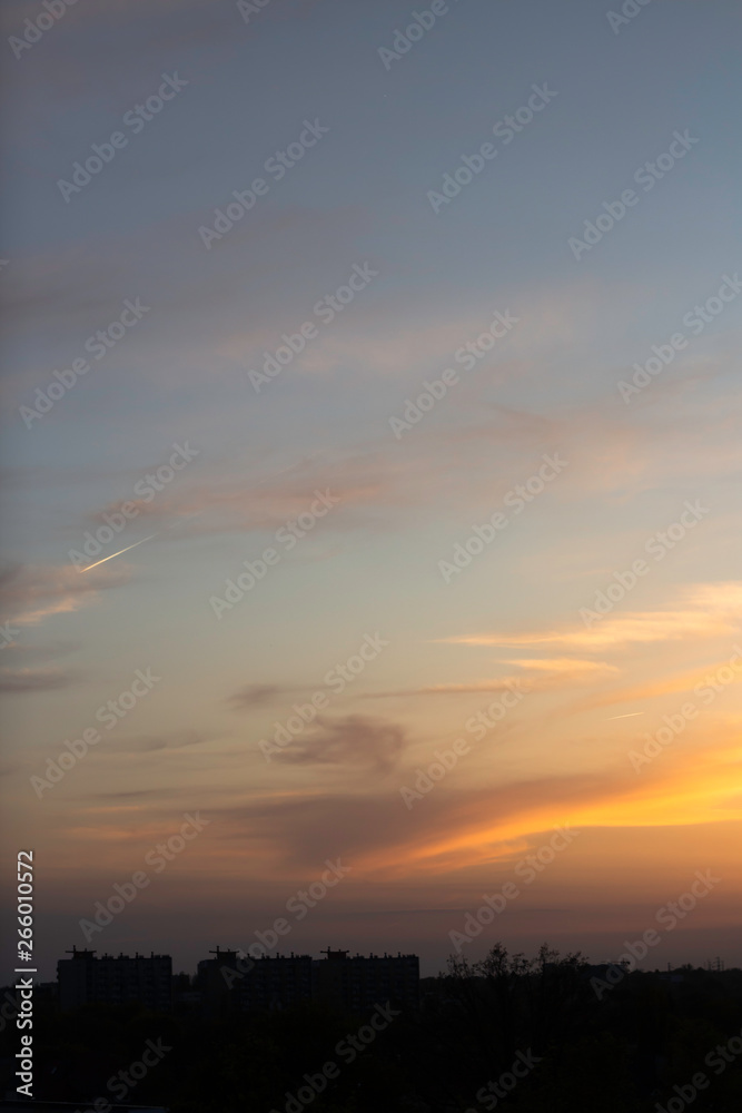 yellow-blue sunset on the background of a dark city with a trace of a flying airplane