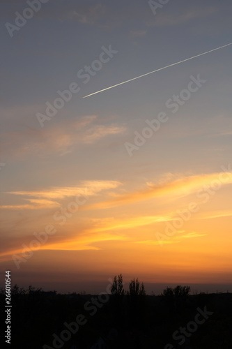 yellow-blue sunset on the background of a dark city with a trace of a flying airplane