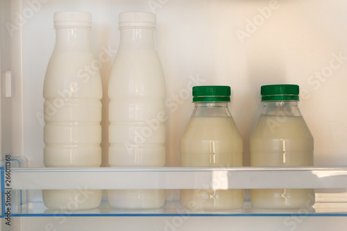 Fermented kefir in refrigerator. White dairy products in plastic bottles on shelf of open empty fridge. Horizontal view.