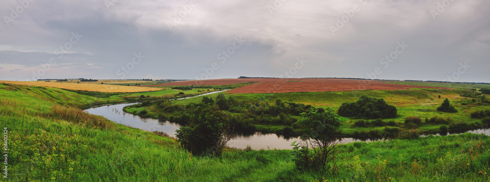 Cloudy summer landscape with river and wheat fields