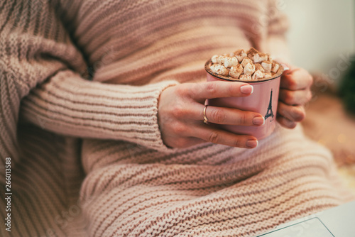 Winter hot drinks. Female hands holding cup of coffee or hot chocolate. Warm pink sweater, home comfort and relax. Christmas holidays, hot drinks and people concept. Toned image. Selective focus.