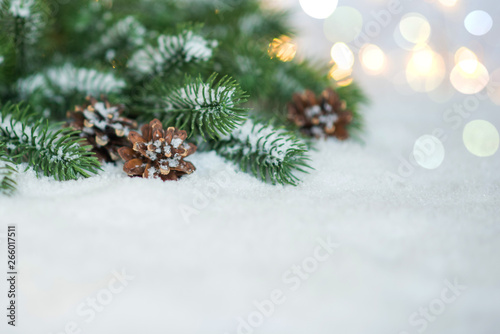 Blurred christmas tree branches, snow and pine cones with twinkling lights. Holiday mock up. Toned image with copy space. Selective focus.