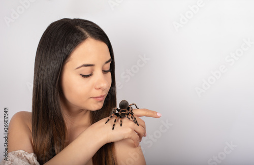 beautiful brunette girl with blue eyes, white background, beauty, on her hands a spider tarantula, looks at the spider and into the camera, close-up photo