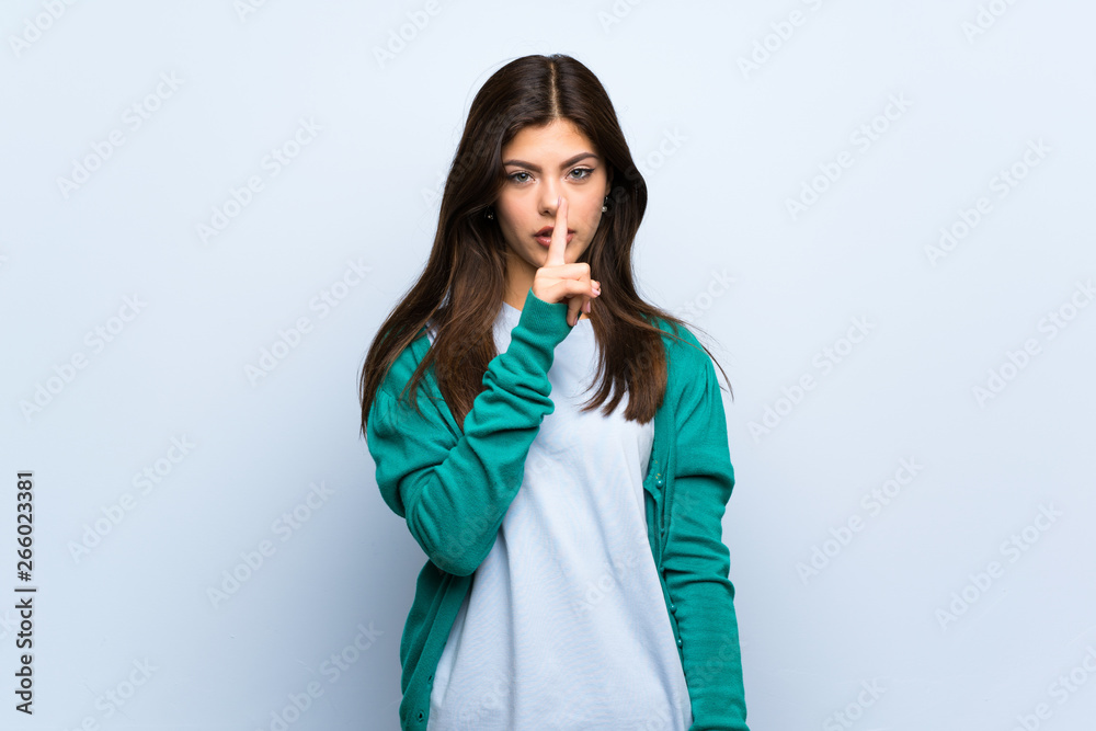 Teenager girl over blue wall showing a sign of silence gesture putting finger in mouth Teenager girl over blue wall showing a sign of silence gesture putting finger in mouth
