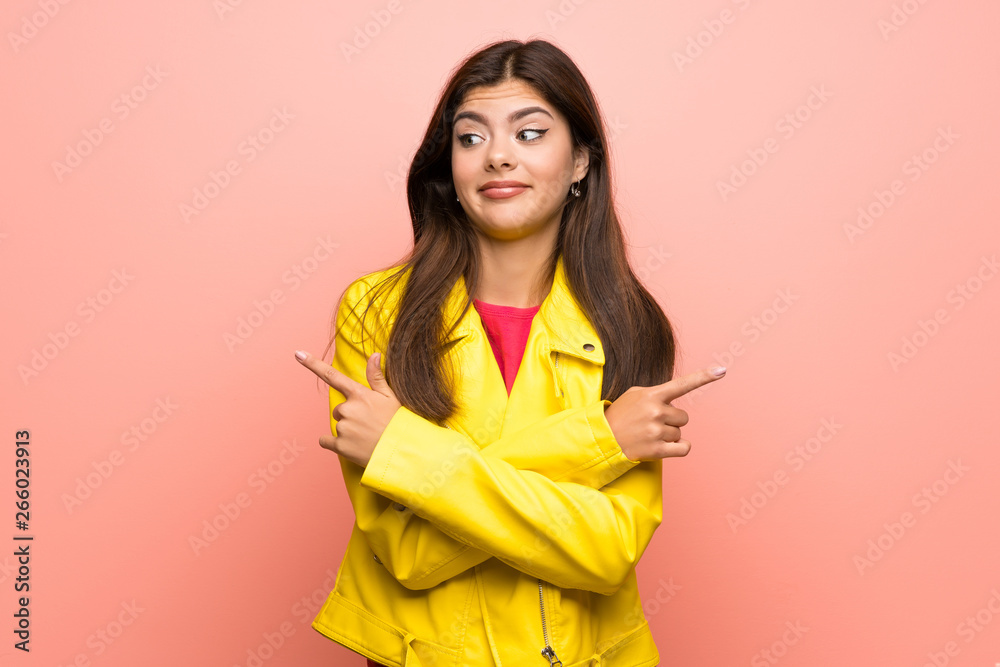 Teenager girl over pink wall pointing to the laterals having doubts Teenager girl over pink wall pointing to the laterals having doubts
