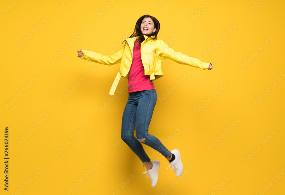 Teenager girl jumping over isolated yellow wall