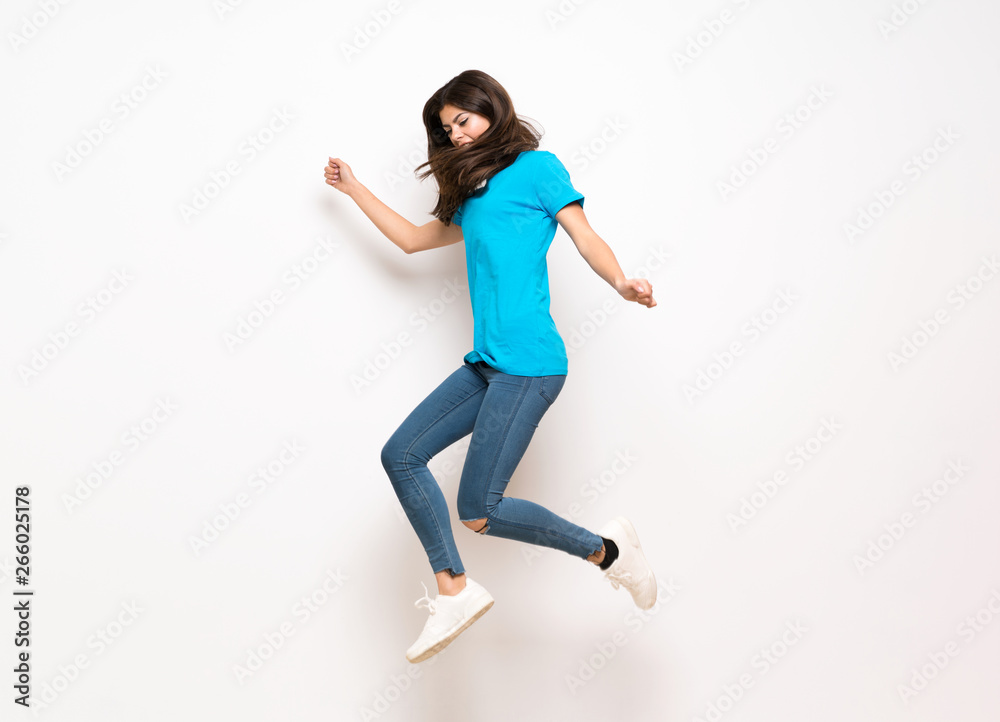 Teenager girl jumping over isolated white wall