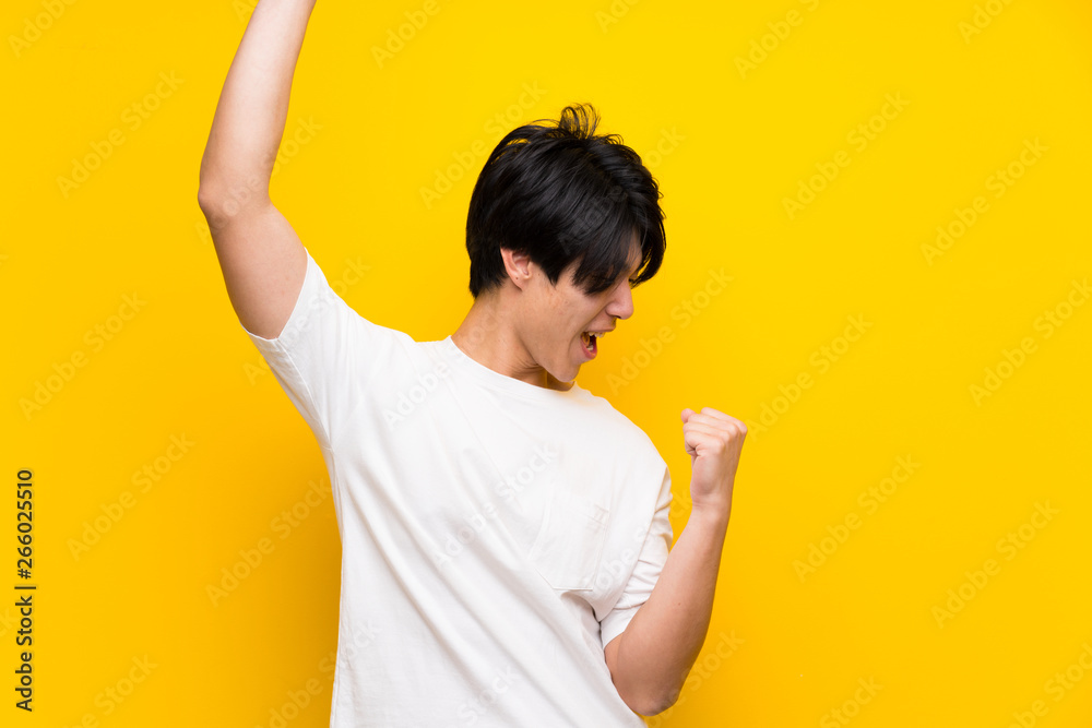 Asian man over isolated yellow wall celebrating a victory
