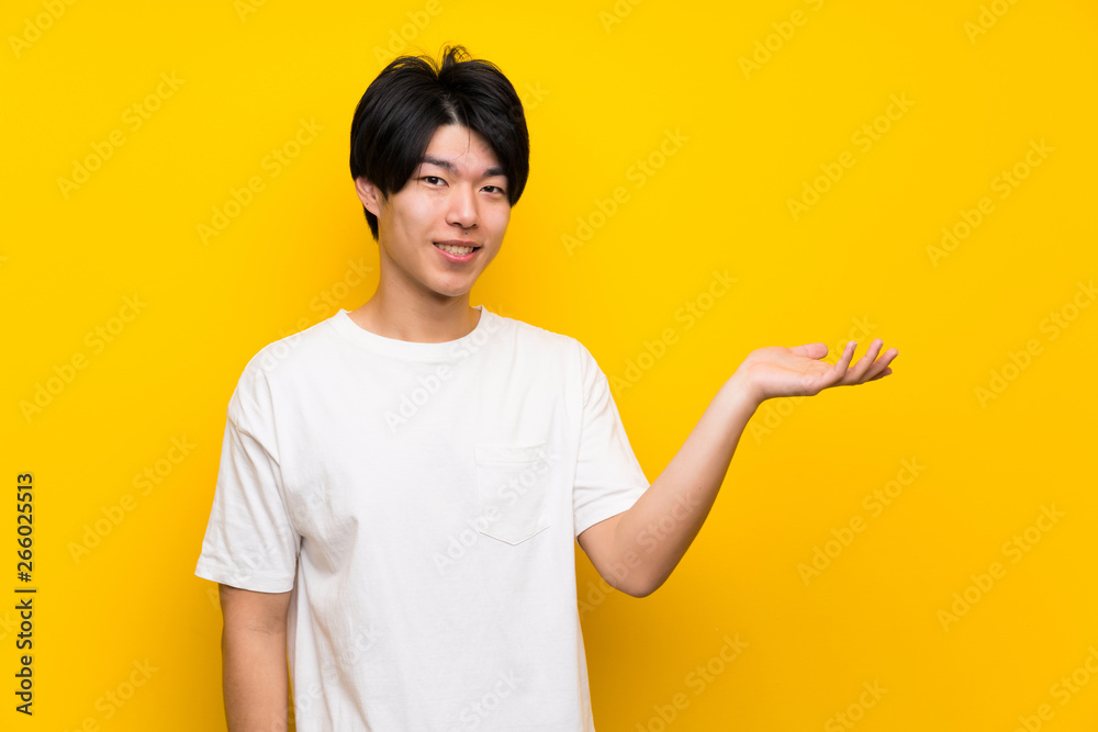 Asian man over isolated yellow wall holding copyspace imaginary on the palm to insert an ad Asian man over isolated yellow wall holding copyspace imaginary on the palm to insert an ad