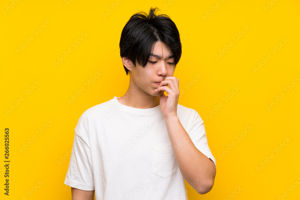Asian man over isolated yellow wall having doubts Asian man over isolated yellow wall having doubts