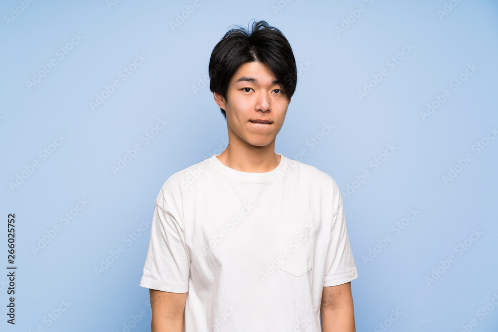 Asian man on isolated blue background having doubts and with confuse face expression Asian man on isolated blue background having doubts and with confuse face expression