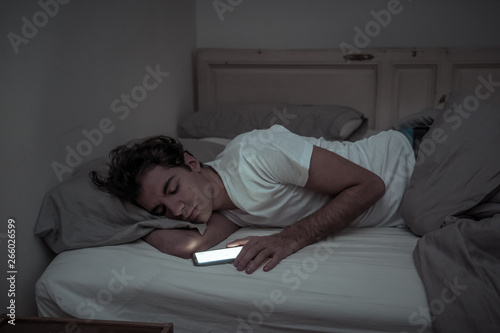 Young man addicted to online social media sleepless surfing on the Internet in bed