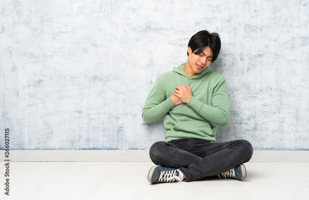 Asian man sitting on the floor having a pain in the heart