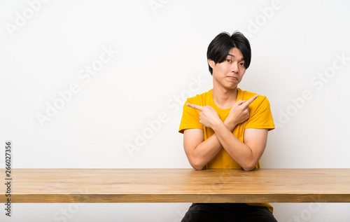 Asian man with yellow shirt pointing to the laterals having doubts © luismolinero