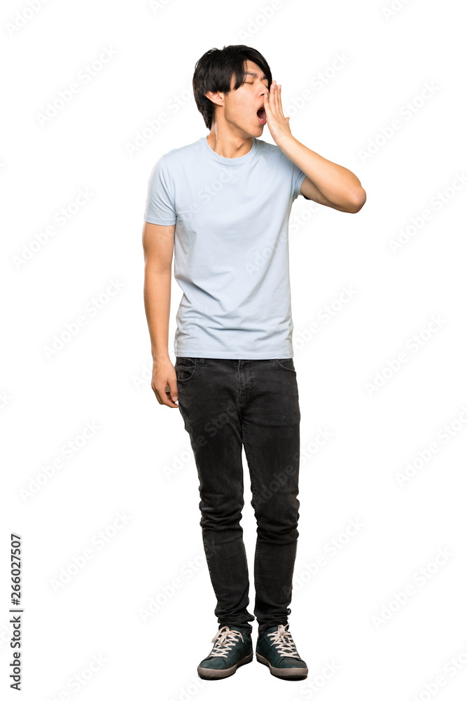 A full-length shot of a Asian man with blue shirt yawning and covering wide open mouth with hand over isolated white background A full-length shot of a Asian man with blue shirt yawning and covering wide open mouth with hand over isolated white background