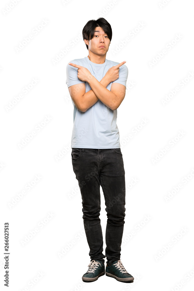 A full-length shot of a Asian man with blue shirt pointing to the laterals having doubts over isolated white background A full-length shot of a Asian man with blue shirt pointing to the laterals having doubts over isolated white background