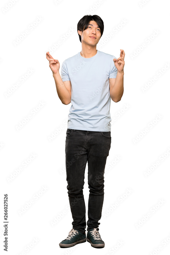 A full-length shot of a Asian man with blue shirt with fingers crossing and wishing the best over isolated white background A full-length shot of a Asian man with blue shirt with fingers crossing and wishing the best over isolated white background
