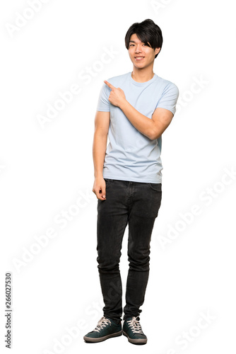 A full-length shot of a Asian man with blue shirt pointing to the side to present a product over isolated white background