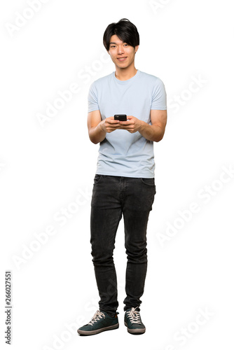 A full-length shot of a Asian man with blue shirt sending a message with the mobile over isolated white background
