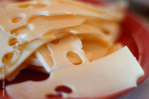 Close-up of several slices of cheese with large holes on a red saucer