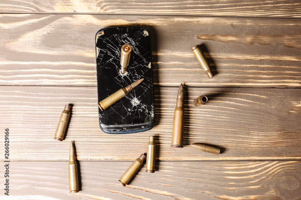 Crashed black smartphone with a bullet on white background. Broken lcd touch screen. Information technology photo. War concept. Crashed black smartphone with a bullet on white background. Broken lcd touch screen. Information technology photo. War concept.