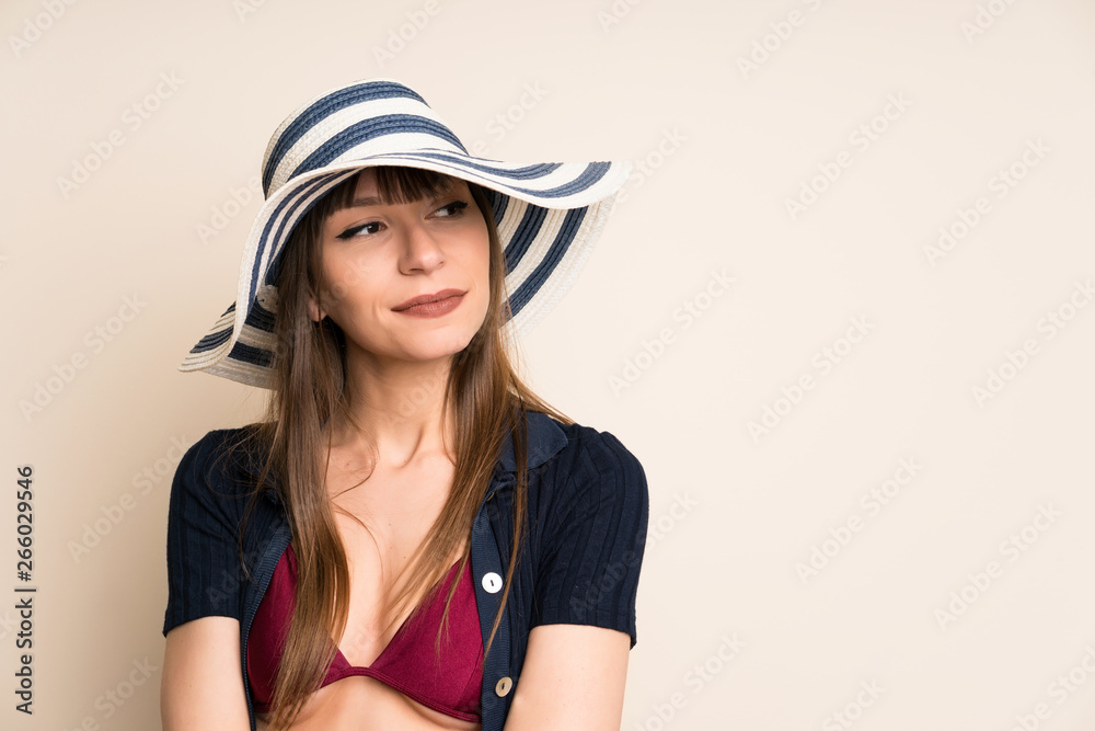 Woman in bikini on ocher background standing and looking to the side Woman in bikini on ocher background standing and looking to the side