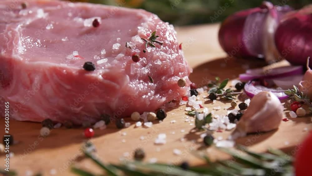 Close-up slow motion footage of strewing salt and pepper at fresh raw beef meat on the desk