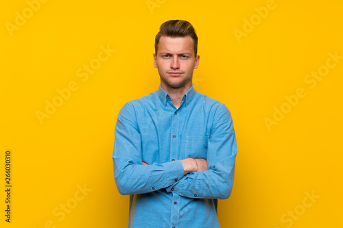Blonde man over isolated yellow wall feeling upset