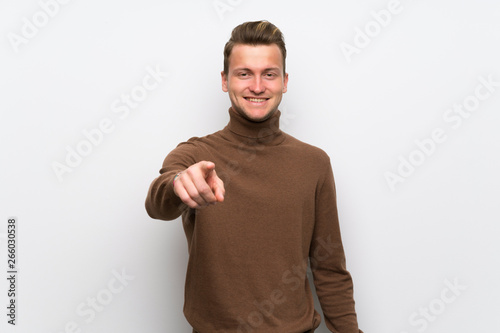 Blonde man over isolated white wall points finger at you with a confident expression