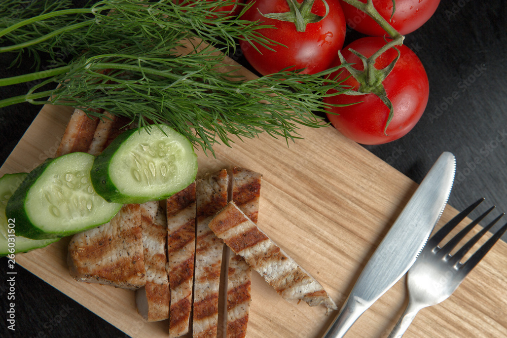 Greens with tomatoes and grilled Turkey steak on a chopping Board. Cutlery on a cutting Board. Top view Greens with tomatoes and grilled Turkey steak on a chopping Board. Cutlery on a cutting Board. Top view