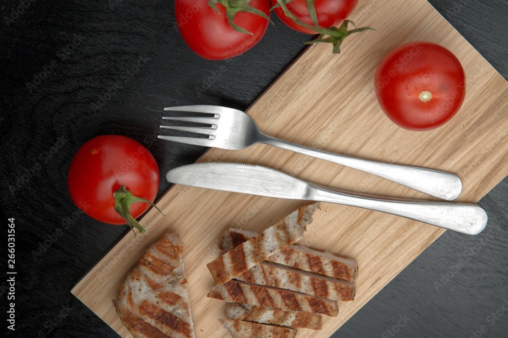 Greens with tomatoes and grilled Turkey steak on a chopping Board. Cutlery on a cutting Board. Top view Greens with tomatoes and grilled Turkey steak on a chopping Board. Cutlery on a cutting Board. Top view