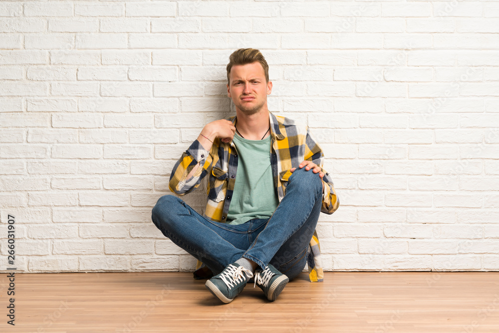 Blonde man sitting on the floor with tired and sick expression