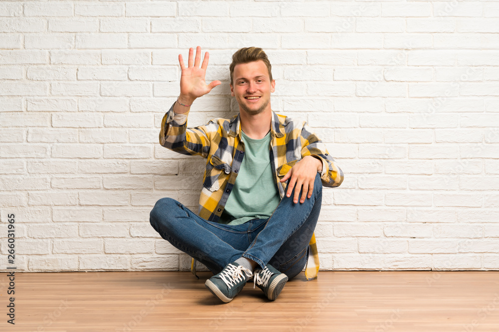 Blonde man sitting on the floor counting five with fingers Blonde man sitting on the floor counting five with fingers