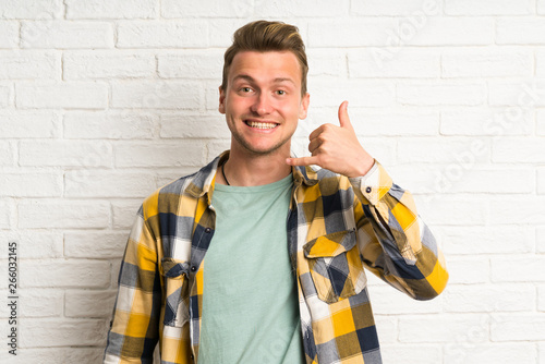 Blonde handsome man over white brick wall making phone gesture