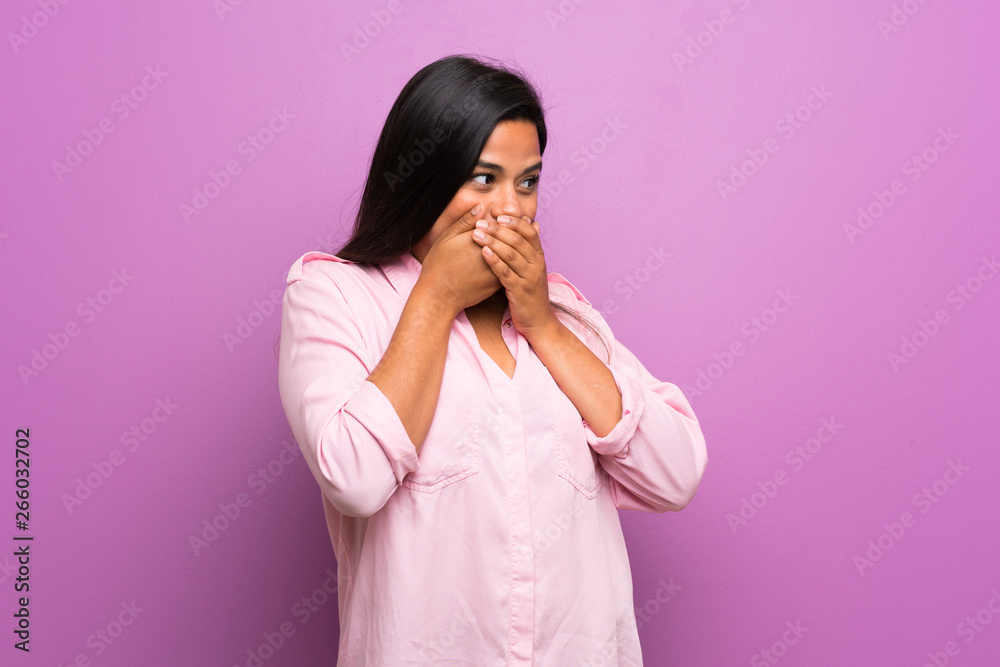 Young Colombian girl over purple wall covering mouth and looking to the side Young Colombian girl over purple wall covering mouth and looking to the side