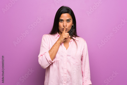 Young Colombian girl over purple wall showing a sign of silence gesture putting finger in mouth