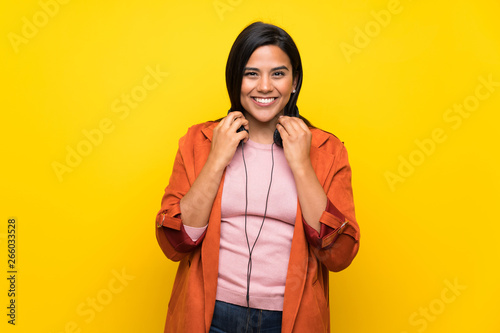 Young Colombian girl over yellow wall with headphones © luismolinero