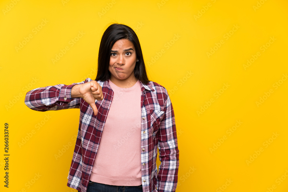 Young Colombian girl over yellow wall showing thumb down sign Young Colombian girl over yellow wall showing thumb down sign