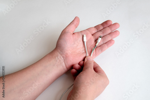 A hand holds two wires with a lightning connector. One wire is working  the other wire is damaged