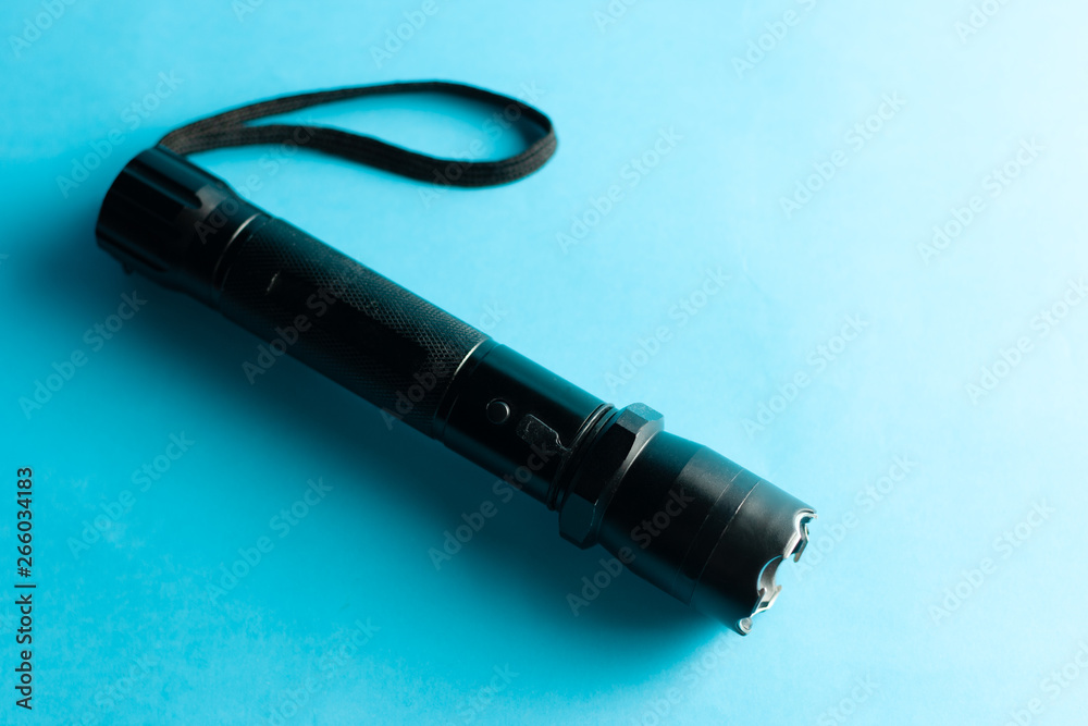 A black metal flashlight with shocker at the blue background. protection and security concept. for design and decoration. A black metal flashlight with shocker at the blue background. protection and security concept. for design and decoration.