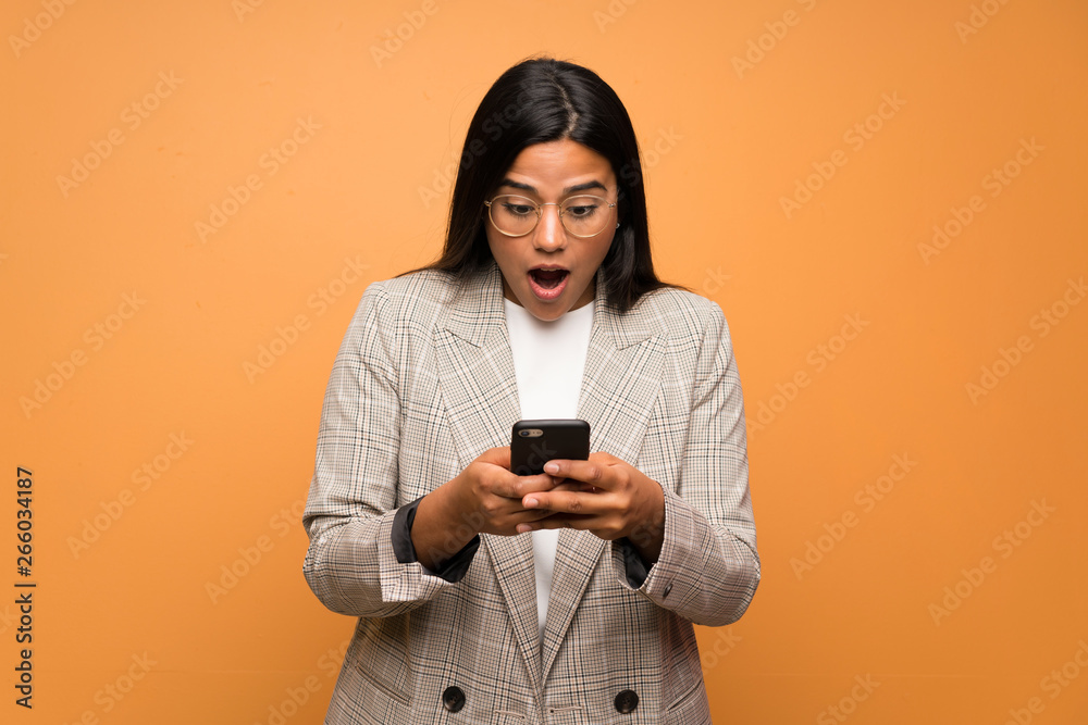 Young Colombian girl over brown wall surprised and sending a message Young Colombian girl over brown wall surprised and sending a message