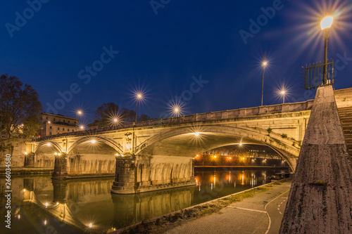 Ponte Sisto bridge and river Tiber at night at the side of the stairs. A stone street bridge in the historic center of Rome at night with illumination. Path at the riverside with lateral view