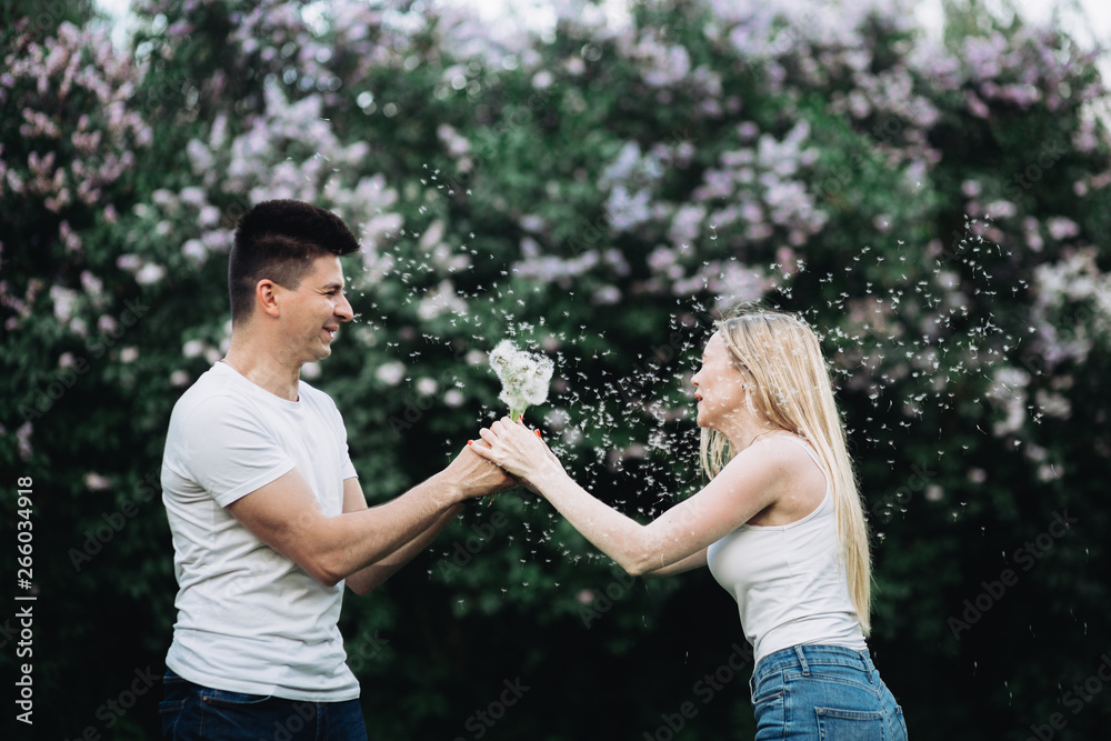A young couple in love holding a dandelion in front of a flowering bush A young couple in love holding a dandelion in front of a flowering bush