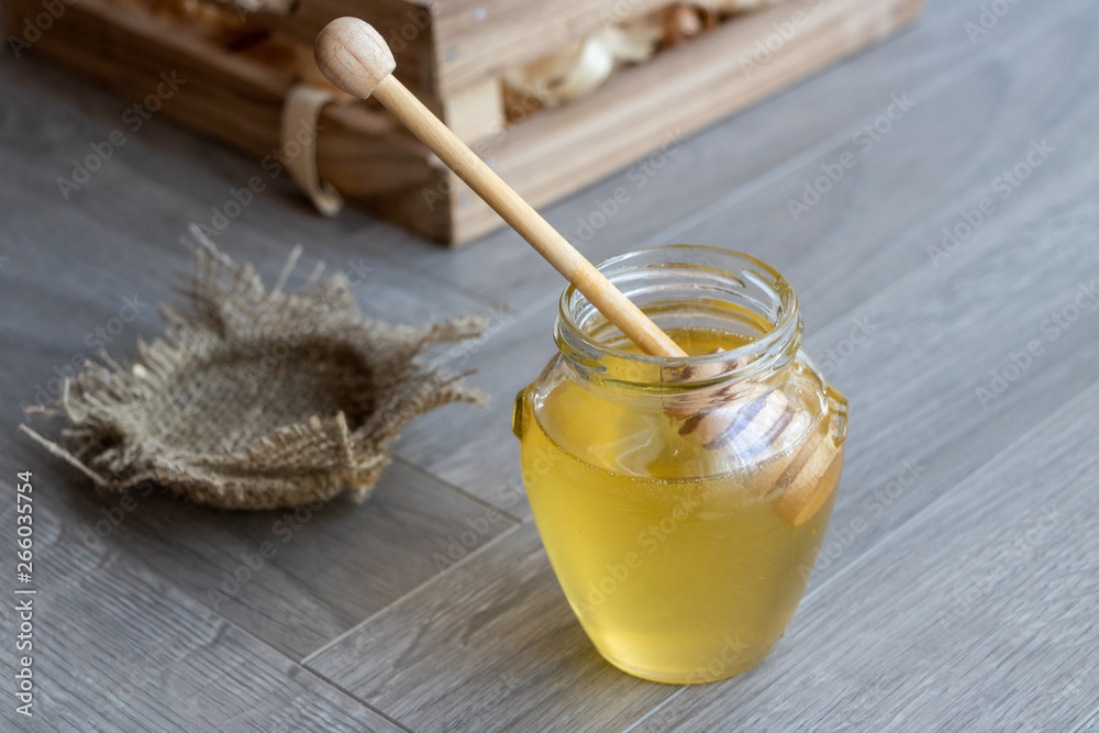 Honey in a glass jar on a gray background. Wooden spoon for honey. Horizontal orientation.
