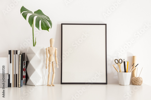 Poster frame mock up and leaf in geometric vase, clock and artisitic tools on white table. Home office decor. photo